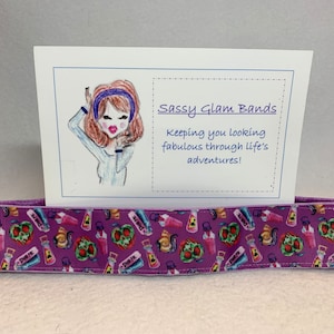 May include: Purple hair tie with a colorful print of potion bottles and skulls. The hair tie is displayed on a white card with the text "Sassy Glam Bands keeping you looking fabulous through life's adventures!"