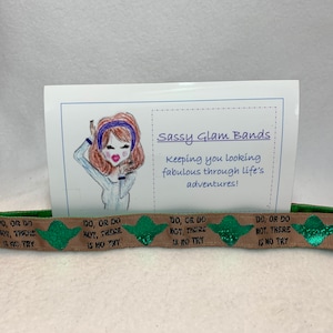 May include: A brown and green hair tie with the text "Do, or do not, there is no try" repeated on it. The hair tie is on a white card with the text "Sassy Glam Bands keeping you looking fabulous through life's adventures!"