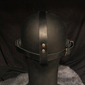 May include: Black leather mask with a strap that goes around the head. The strap has two brass rivets and a buckle.