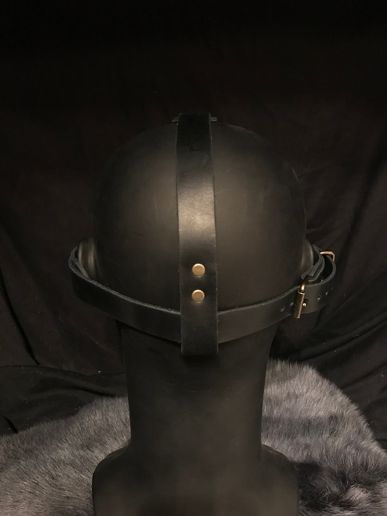 May include: Black leather mask with a strap that goes around the head. The strap has two brass rivets and a buckle.