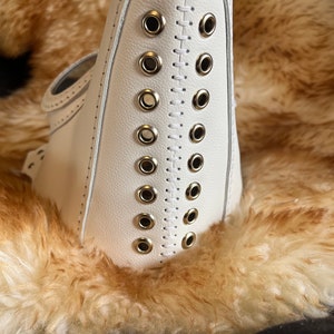 May include: White leather mask with a row of silver eyelets and stitching down the center.