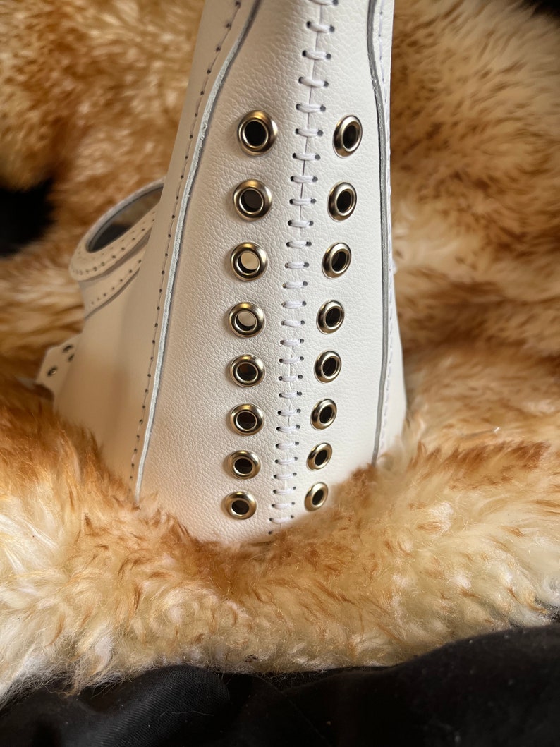 May include: White leather mask with a row of silver eyelets and stitching down the center.