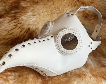 May include: White leather plague doctor mask with silver studs and clear eye lenses. The mask has a long beak and a strap that goes around the head.