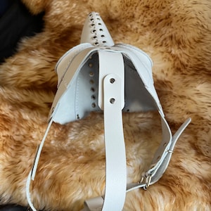 May include: White leather mask with a pointed nose and studded details. The mask has a strap that goes around the head.