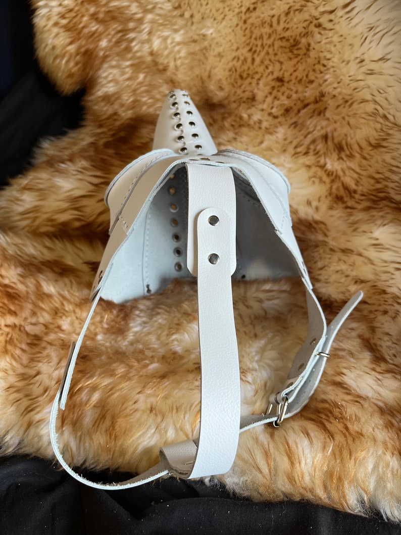 May include: White leather mask with a pointed nose and studded details. The mask has a strap that goes around the head.