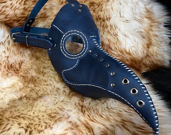 May include: A blue leather plague doctor mask with a long beak, eye holes, and a clear plastic window. The mask has a strap for wearing.
