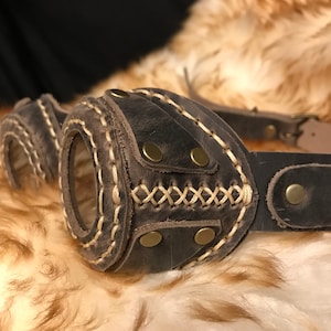 May include: Brown leather steampunk goggles with gold rivets and stitching. The goggles have a round lens and are attached to a leather strap.
