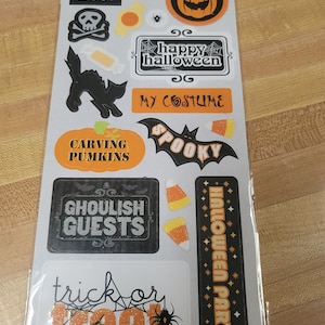May include: A sheet of Halloween-themed glitter stickers with various designs, including pumpkins, bats, candy corn, a spider, a black cat, and signs that say "BOO!", "Happy Halloween", "My Costume", "Carving Pumpkins", "Spooky", "Ghoulish Guests", "Halloween Party", and "Trick or Treat".