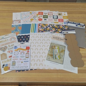 May include: A collection of scrapbook supplies, including patterned paper, stickers, and die-cut shapes. The paper features floral, rainbow, and geometric designs. Stickers include phrases like "Hello" and "Better Together."