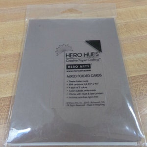 May include: A package of Hero Hues Mixed Folded Cards by Hero Arts. The package contains 12 folded cards, 80lb cardstock, A2 size, 5 1/2 inches by 4 inches. The cards are available in 3 colors, with color on the outside and white on the inside. The cards are archival, acid-free, and lignin-free. They are compatible with inkjet and laser printers.