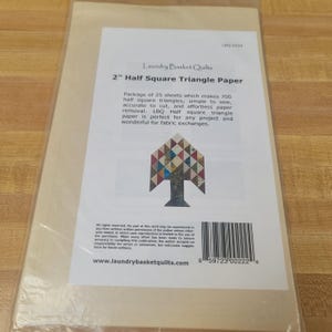 May include: Package of 25 sheets of 2" Half Square Triangle Paper by Laundry Basket Quilts. The package makes 700 half square triangles. The package includes a tree-shaped graphic with a colorful patchwork design.