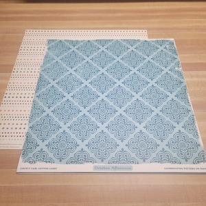 May include: Two sheets of patterned paper. One sheet has a light blue floral design, and the other has a dotted pattern in pink and gold. The bottom sheet has the text "COUNTY FAIR: COTTON CANDY" and "October Afternoon".