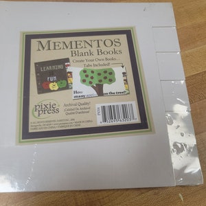 May include: A white package with a colorful image of a book with the text "Learning is Fun" and a tree with apples. The package is for Mementos Blank Books, which are archival quality and made in China. The text on the package says "Create Your Own Books... Tabs Included!" and "How many apples on the tree?"