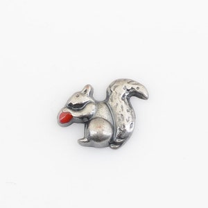 May include: A silver charm in the shape of a squirrel holding a red acorn.