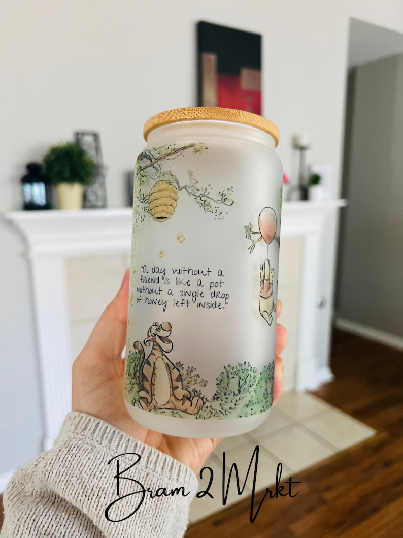 May include: A frosted glass water bottle with a bamboo lid featuring a Winnie the Pooh illustration and the quote "A day without a friend is like a pot without a single drop of honey left inside."