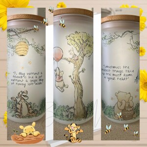 May include: Three Winnie the Pooh themed glass jars with bamboo lids. Each jar features a different Winnie the Pooh quote and illustration. The first jar has a quote about friendship, the second jar has a quote about the smallest things taking up the most room in your heart, and the third jar has a quote about honey.