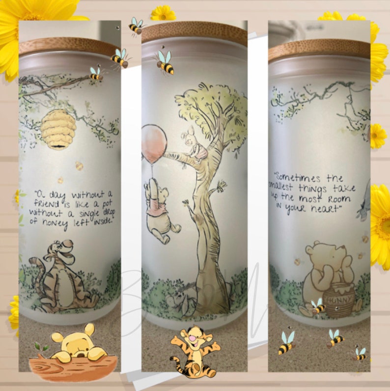 May include: Three Winnie the Pooh themed glass jars with bamboo lids. Each jar features a different Winnie the Pooh quote and illustration. The first jar has a quote about friendship, the second jar has a quote about the smallest things taking up the most room in your heart, and the third jar has a quote about honey.