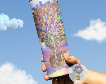 May include: A stainless steel tumbler with a colorful design of a house floating in the air with balloons. The tumbler has a straw and a blue lid. The design is inspired by the movie Up.