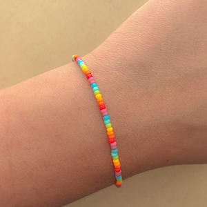 Puede incluir: Un brazalete de cuentas de arcoíris con pequeñas cuentas de colores.