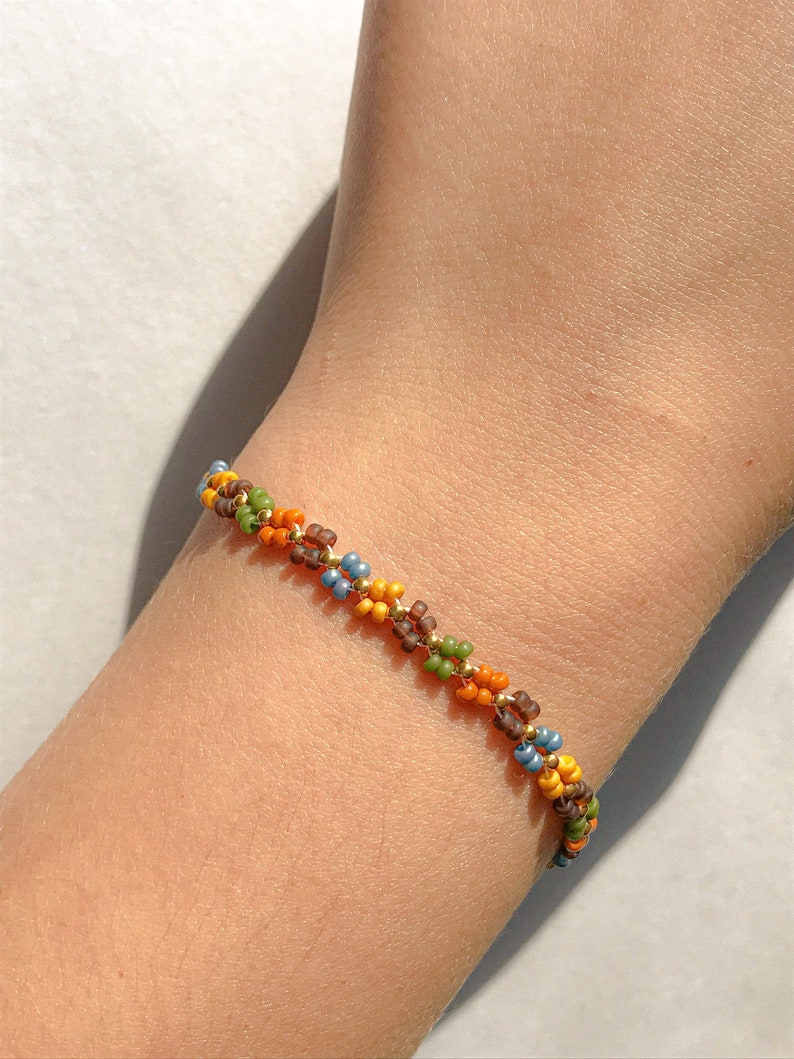 May include: A multi-coloured beaded bracelet with brown, orange, green, and blue beads. The bracelet is woven in a braided pattern.