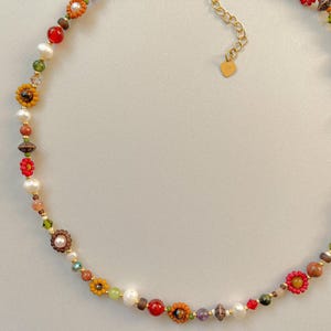 May include: A colorful beaded necklace featuring a variety of beads in shades of red, yellow, green, and brown. The necklace includes flower-shaped beads, pearls, and a gold-colored chain with a heart-shaped charm.