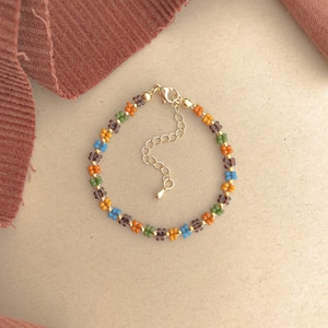 May include: A beaded bracelet with a gold chain clasp. The beads are small and colourful, with shades of brown, orange, blue, and green.