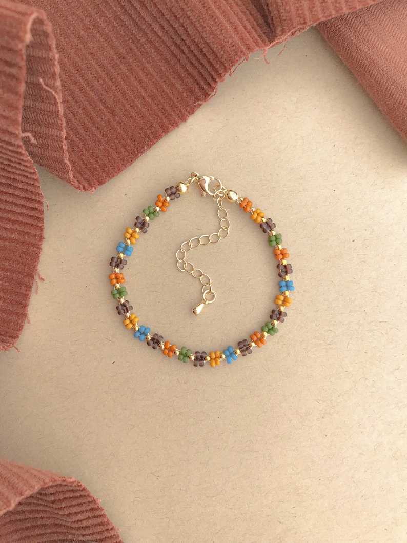 May include: A beaded bracelet with a gold chain clasp. The beads are small and colourful, with shades of brown, orange, blue, and green.