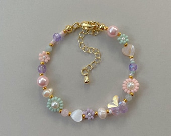May include: A delicate bracelet featuring a mix of pastel-colored beads, including flowers, pearls, and a butterfly charm. The bracelet has a gold chain closure.