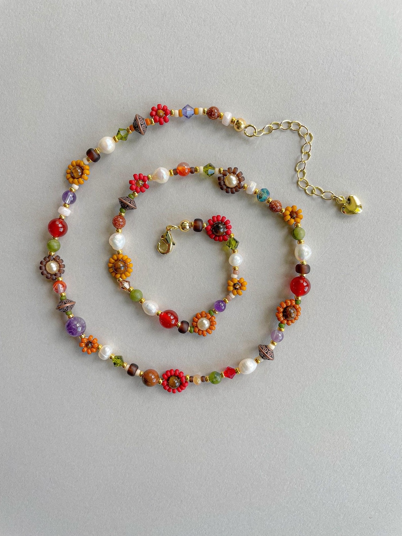 May include: A colorful beaded necklace and bracelet set. The necklace and bracelet feature a variety of beads, including pearls, red and orange beads, and flower-shaped beads. The necklace has a gold-colored chain and clasp.