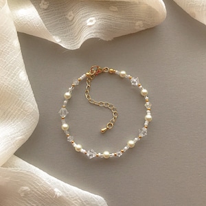 May include: A delicate gold bracelet with a chain closure, featuring small white pearls and clear crystal beads.