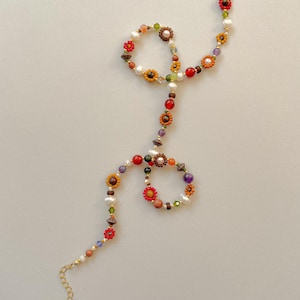 May include: A colorful beaded necklace with a floral design. The necklace features a variety of beads in red, orange, yellow, green, and purple. The necklace has a gold-colored chain and clasp.
