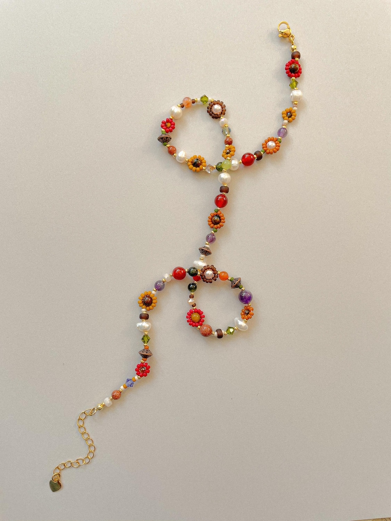 May include: A colorful beaded necklace with a floral design. The necklace features a variety of beads in red, orange, yellow, green, and purple. The necklace has a gold-colored chain and clasp.
