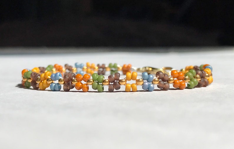May include: A multi-coloured beaded bracelet with brown, orange, yellow, green and blue beads. The bracelet has a gold clasp.