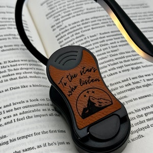May include: A black book light with a brown leather clip. The clip has a mountain design and the text "To the stars who listen".