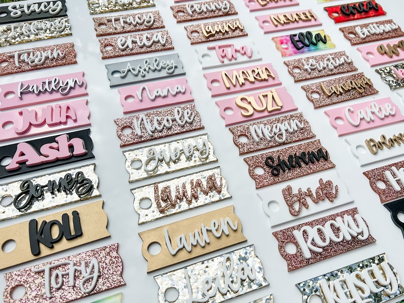 Op de afbeelding: Een verzameling gepersonaliseerde naamstickers met glitter en verschillende kleuren. De stickers zijn gemaakt van hout en plastic en hebben een gat om op te hangen. Sommige van de namen zijn Stacy, Tracy, Penny, Erica, Laura, Ashley, Nana, Maria, Kustin, Lan, Ash, Nicole, Suzi, Megan, Sherena, Bride, Rocky en Kessev.
