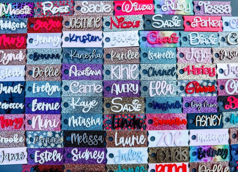 May include: A collection of personalized name tags in various colors and glitter finishes. Each tag features a different name in a decorative font, with a small hole on each end. The tags are arranged in a grid pattern.