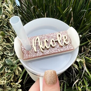 Op de afbeelding: Een witte tumbler met een roze glitterdeksel en een gouden naamplaatje met de tekst "Nicole".