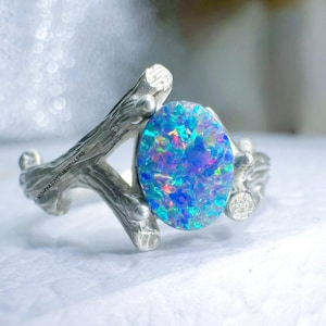 Könnte beinhalten: Ein silberner Ring mit einem großen, ovalen Opal-Edelstein. Der Opal zeigt ein lebendiges Farbspiel mit Blau-, Grün- und Rottönen. Der Ring hat ein einzigartiges, astähnliches Design.