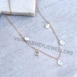 May include: A gold chain necklace with five dangling, irregularly shaped, clear gemstones. The necklace is on a white surface.