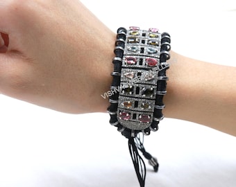 May include: A multi-colored gemstone bracelet with a black cord and silver accents. The bracelet features various rectangular and oval-shaped gemstones in shades of pink, green, and yellow. The bracelet is secured with a black cord and silver clasps.