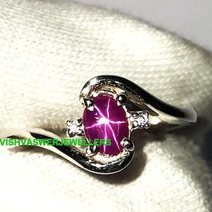 Peut inclure: Une bague en argent avec une pierre précieuse en rubis étoilé rose et deux diamants plus petits. La bague a une bande incurvée.