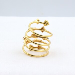 May include: A gold-colored spiral ring with small red and green gemstones. The ring has a unique design with multiple coils and decorative elements. The ring is a piece of jewelry.