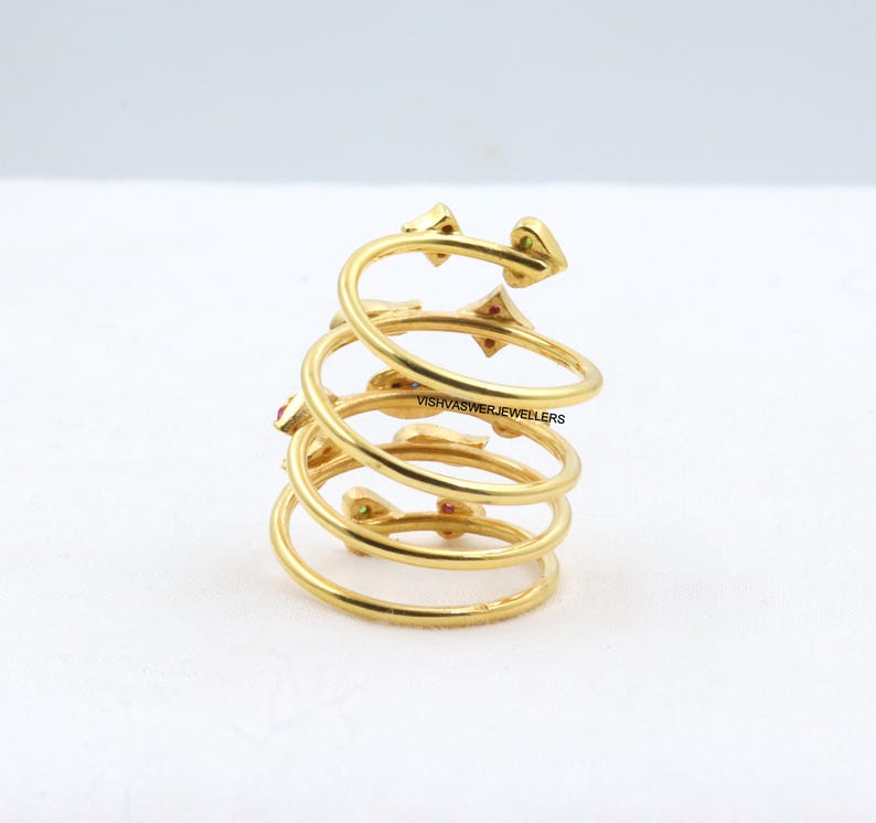May include: A gold-colored spiral ring with small red and green gemstones. The ring has a unique design with multiple coils and decorative elements. The ring is a piece of jewelry.