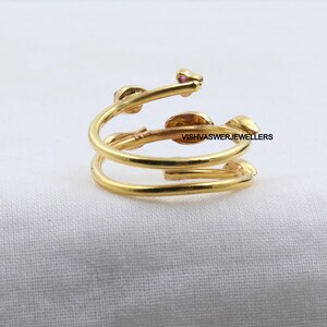 Pu&ograve; includere: Un anello color oro con un design a spirale. L'anello presenta piccoli dettagli a forma di foglia e minuscole pietre preziose rosa. Il testo "VISHVASWERJEWELLERS" &egrave; visibile sull'anello.