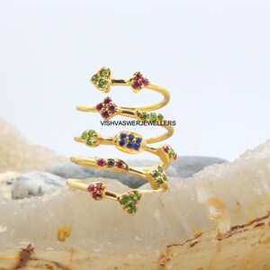 May include: A gold-colored spiral ring with multiple bands, each adorned with colorful gemstones. The gemstones are arranged in clusters of red, green, and blue. The text "VISHVASWERJEWELLERS" is visible on the ring.