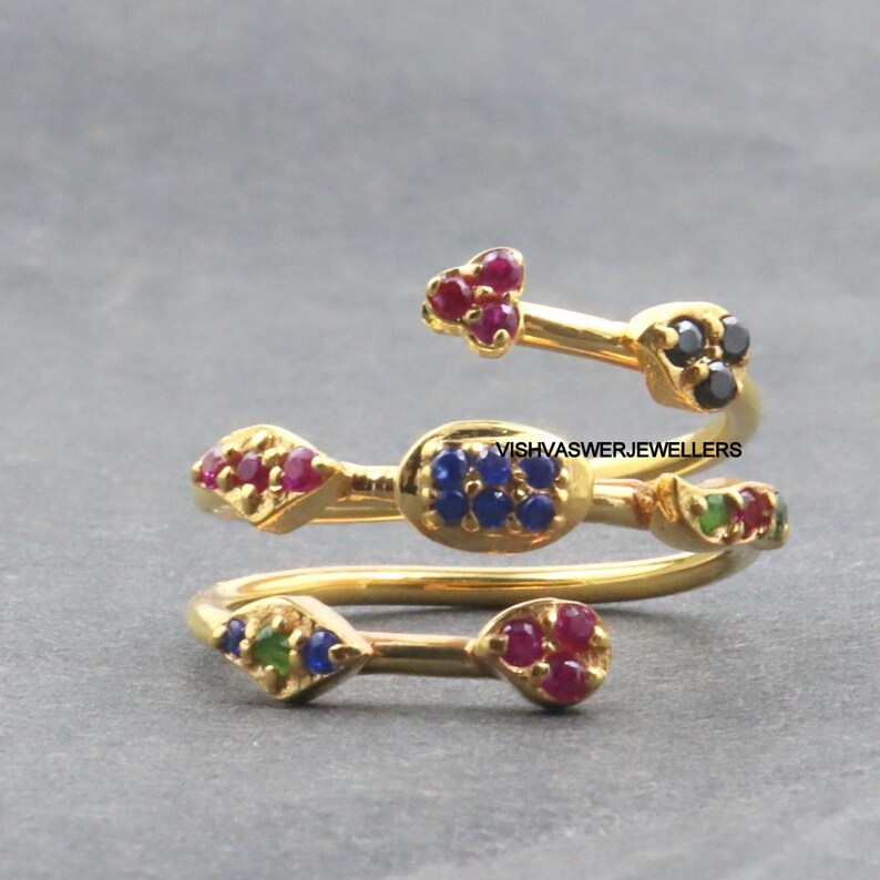 Pu&ograve; includere: Un anello a spirale dorato con molteplici accenti di pietre preziose. L'anello presenta pietre preziose rosse, blu, verdi e nere. Il design dell'anello include una serie di fasce curve che si avvolgono attorno al dito.