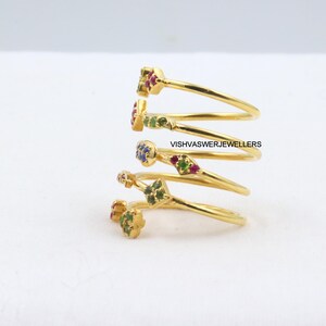 May include: Gold-toned spiral ring with colorful gemstones. The ring features a unique design with multiple loops, each adorned with small, vibrant gemstones in red, green, and blue. The text "VISHVASWERJEWELLERS" is visible.