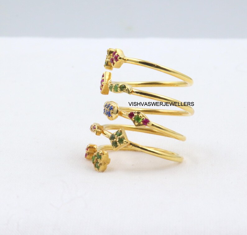 May include: Gold-toned spiral ring with colorful gemstones. The ring features a unique design with multiple loops, each adorned with small, vibrant gemstones in red, green, and blue. The text "VISHVASWERJEWELLERS" is visible.