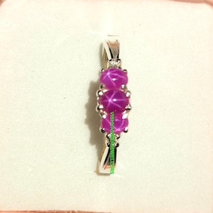 Op de afbeelding: Een zilveren ring met drie ronde, roze sterrobijn edelstenen. De edelstenen zijn in een rij geplaatst, met een kleine accentsteen aan de bovenkant. De ring wordt gepresenteerd op een wit oppervlak.