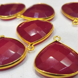 May include: Eight red gemstone pendants with gold-toned metal settings. The pendants are teardrop shaped and have a faceted design.